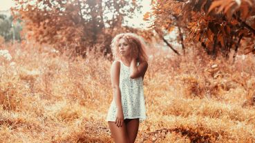 A woman in a forest in a short white dress touching her hair